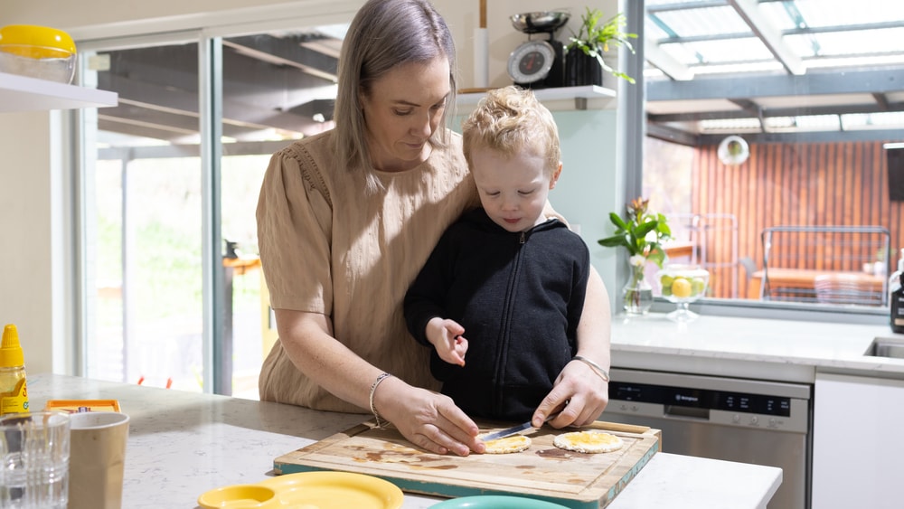 Parent assisting child preparing food in the kitchen at home.