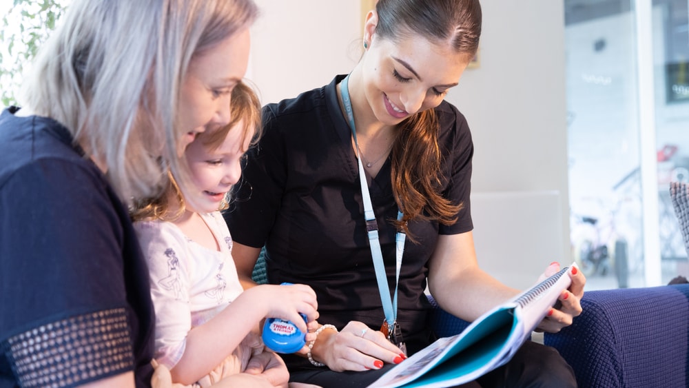 QEC clinician showing printed educational resource to parent and child during home visit.