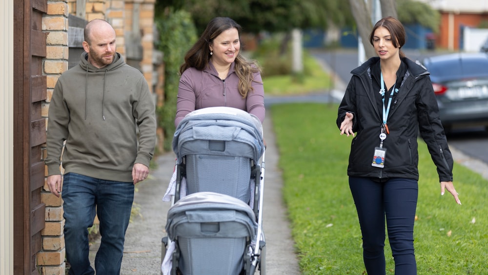 QEC clinician working and talking with parents as they push pram down the street.