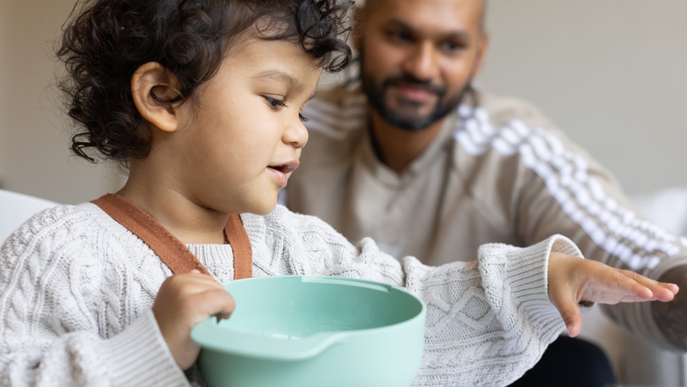 Child playing with toys, parent watching in background.