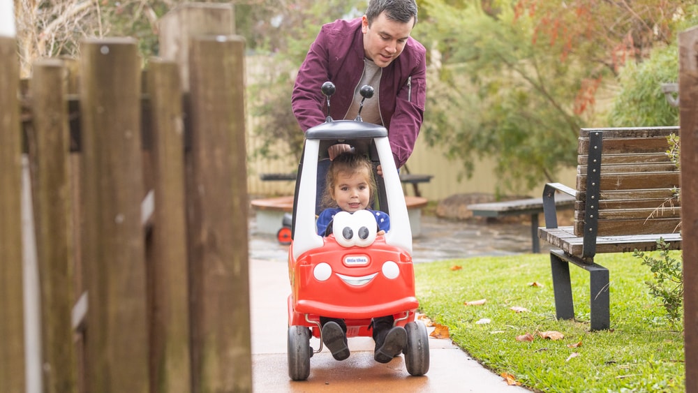 Parent pushing child in car around sensory garden