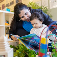 Parent reading book to toddler in QEC PlayRoom.