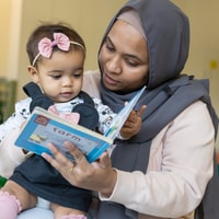 Parent reading booking with toddler in QEC PlayRoom.