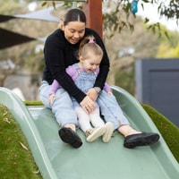 Parent and child going down slide together in QEC sensory garden.