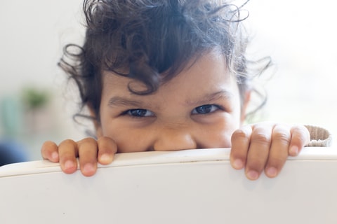 Child looking over back of chair and smiling.