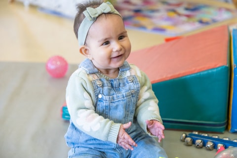 Baby sitting on QEC PlayRoom floor clapping.