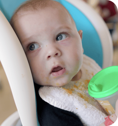 Baby in feeding chair with sippy cup in QEC residential kitchen