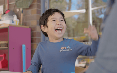 Toddler laughing with QEC clinician in QEC sensory garden.
