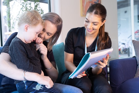 QEC clinician showing printed educational resource to parent and child during home visit.