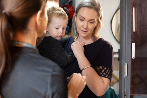 QEC clinician on a home visit to a family. Parent at the front door holding child, QEC clinician showing parent their QEC identification.