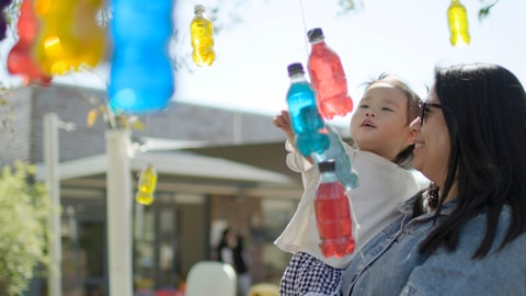 Parent holding toddler looking at bottles in the sensory garden