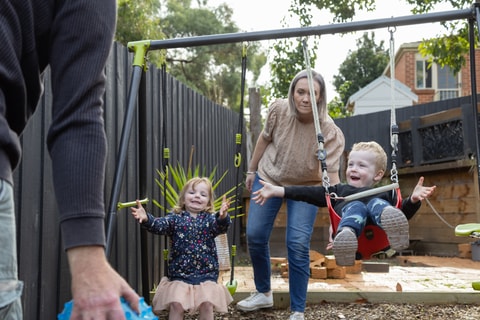 Parent pushing child on a swing in backyard.