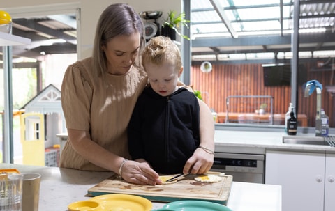 Parent helping child prepare food in kitchen.