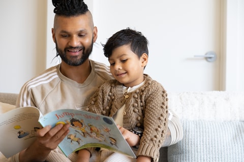 Dad reading a book to child and smiling.