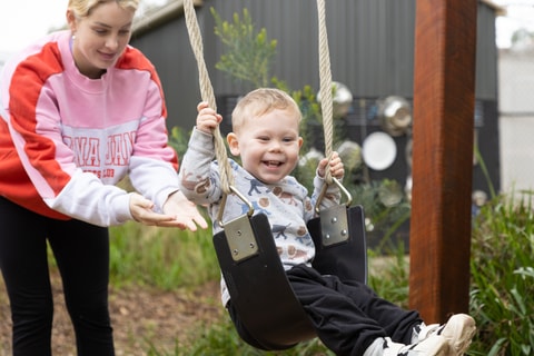 Parent pushing child on swing in QEC sensory garden.