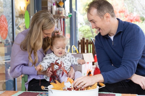 Two parents holding toddler and playing with leaves in the QEC sensory garden.