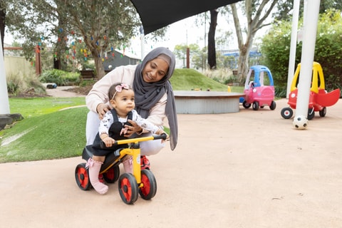 Parent holding child while child practices riding a bike in QEC sensory garden.
