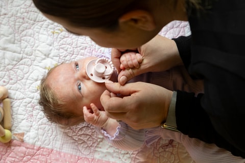 Baby laying on back with dummy in mouth, parent leaning over and looking at baby.