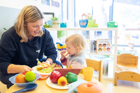 Parent and child playing with toy food in play kitchen in QEC PlayRoom.